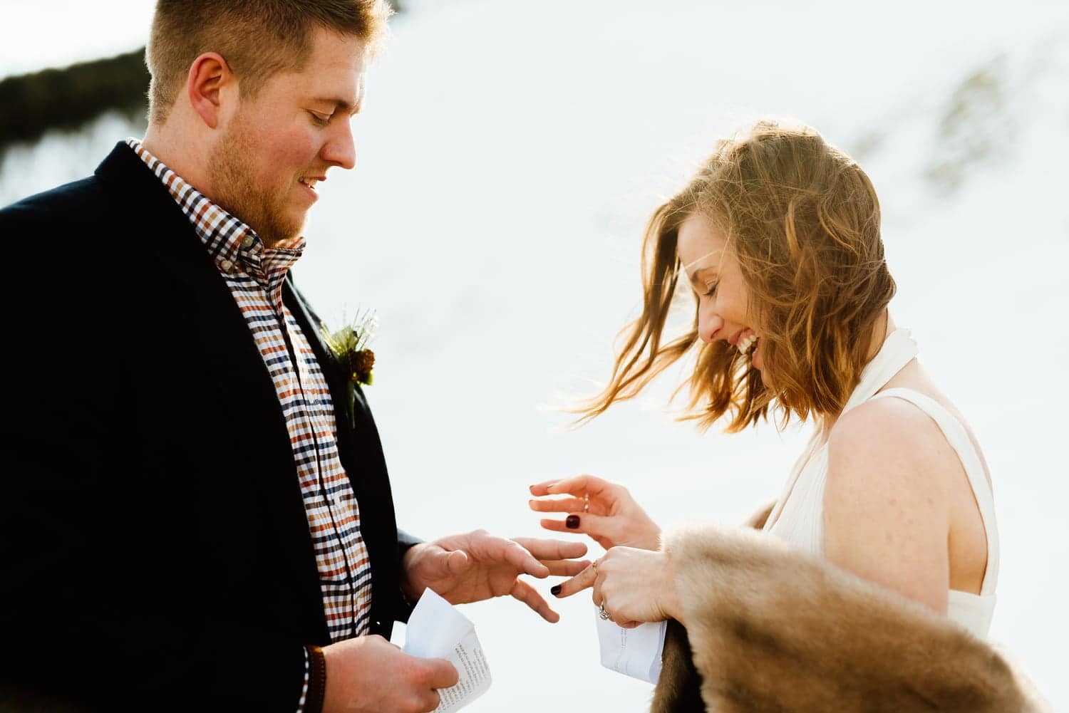Bride places ring on grooms finger, while smiling, during intimate elopement ceremony. 