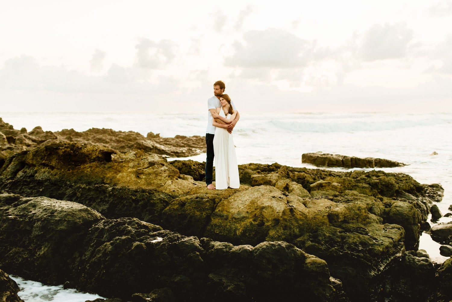 Bride and groom embrace on rocks along the shore in Santa Teresa, Costa Rica.