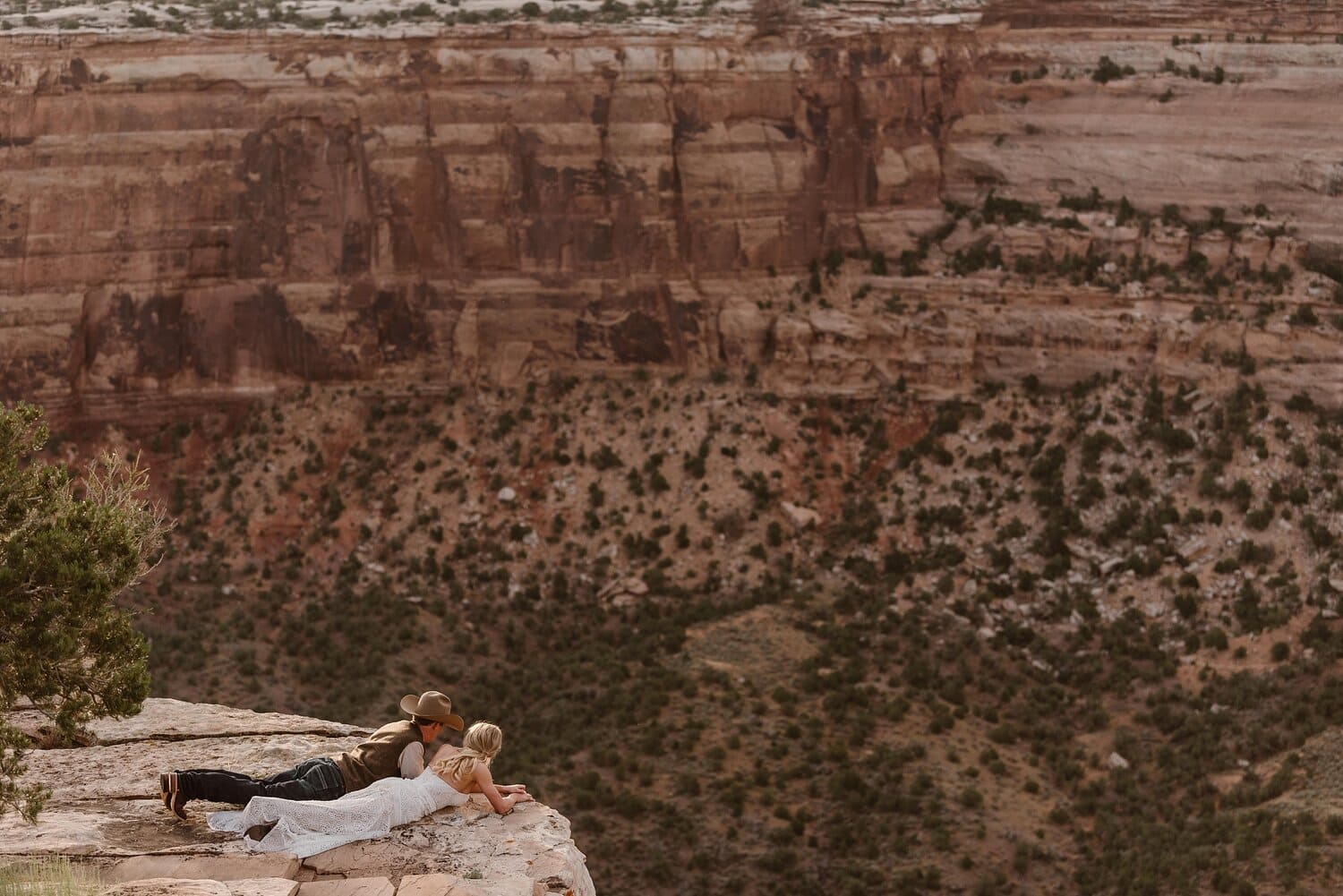 Bride and groom lay down on cliff and overlook the red rocks at Colorado National Monument. 