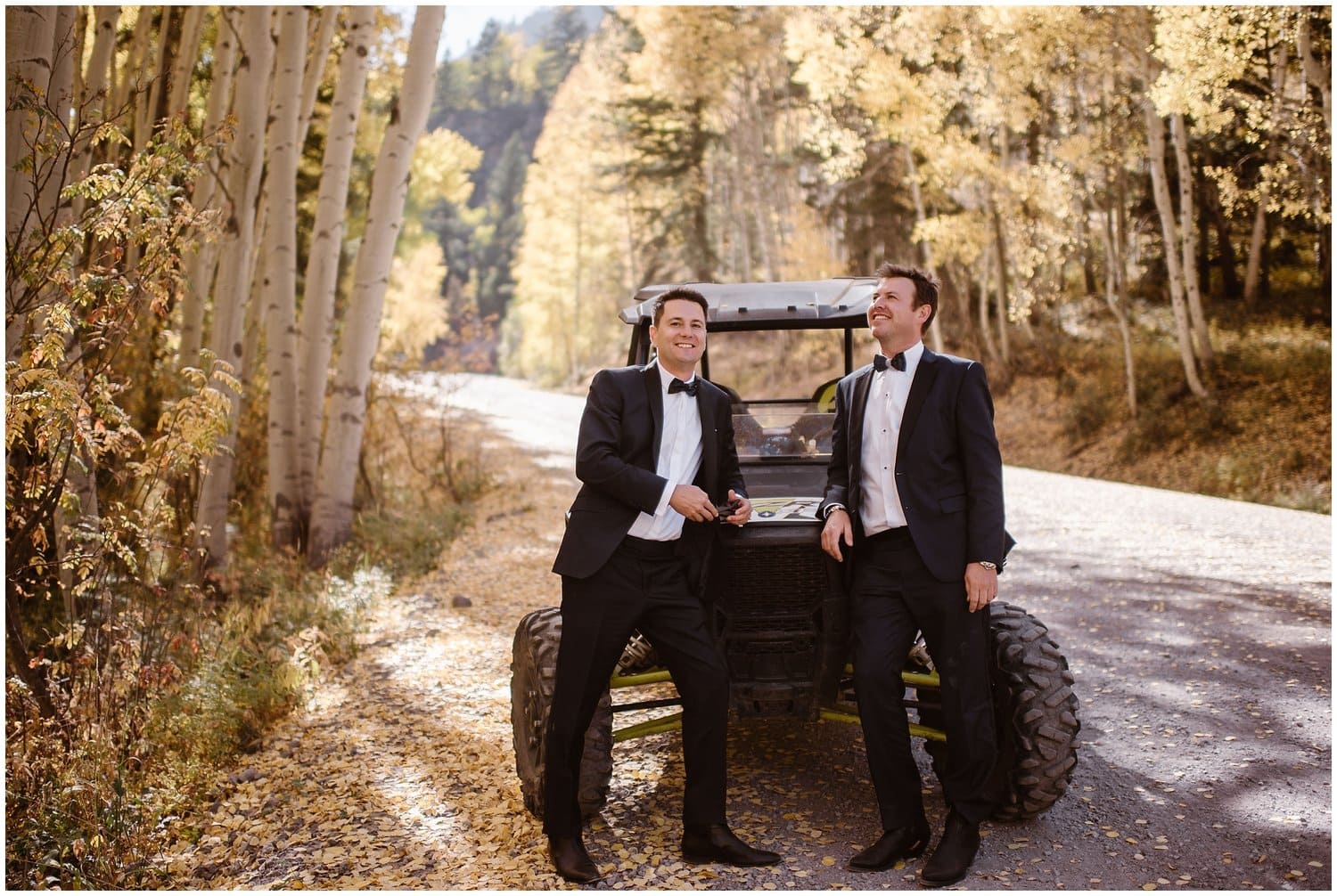 Grooms stand in front of UTA on road lined with aspens in Ouray, Colorado. 