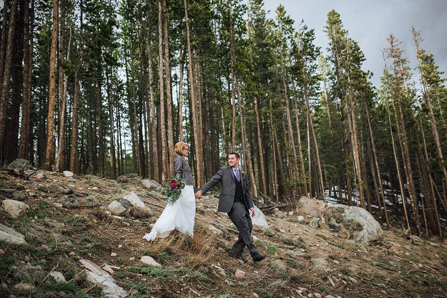 Bride and groom hike down a hill together in Rocky Mountain National Park, Colorado. 