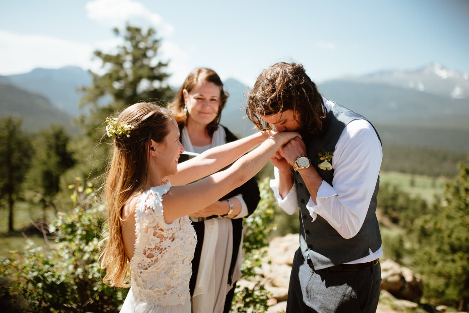 Groom kisses bride's hands during intimate elopement ceremony at 3M Curve in Rocky Mountain National Park, Colorado. 