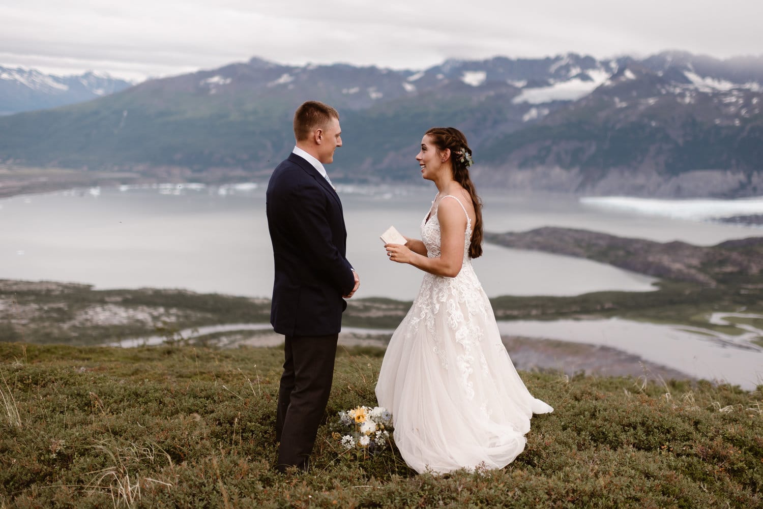 Bride and groom exchange rings and say their vows during intimate elopement ceremony, in front of a glacial lake, in Alaska. 