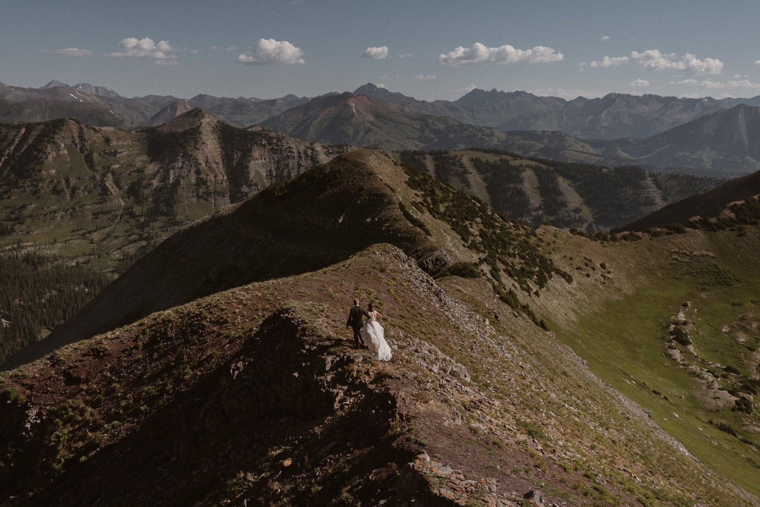 Wide shot of a bride and groom standing on a mountain landscape on their elopement day.
