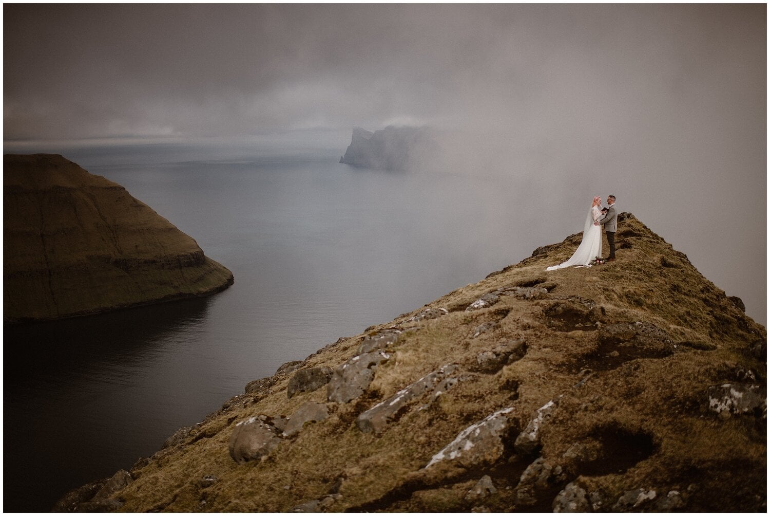 Bride and groom read vows, with fog in background, at Faroe Islands. 