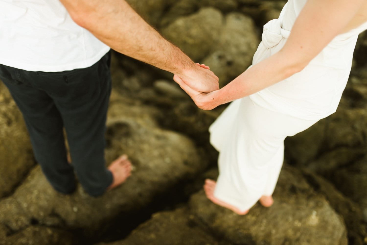 Close up of bride and groom holding hands while standing on rocks along the shore in Santa Teresa, Costa Rica.