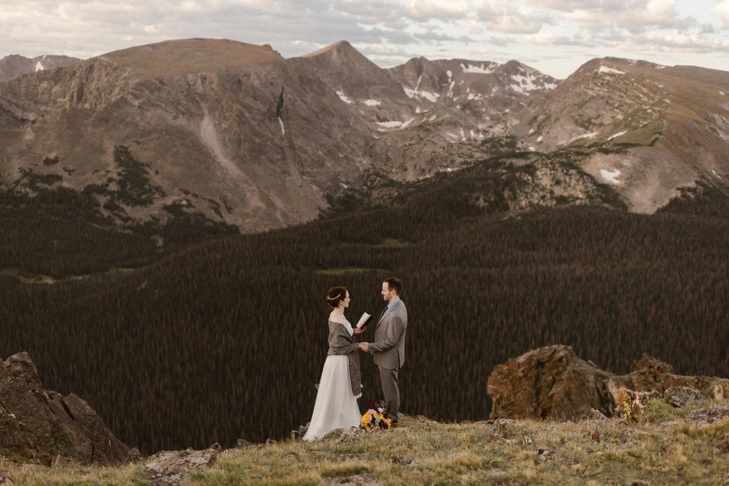 Bride reads her vows to the groom and they are holding hands during their intimate elopement ceremony in the mountains. 