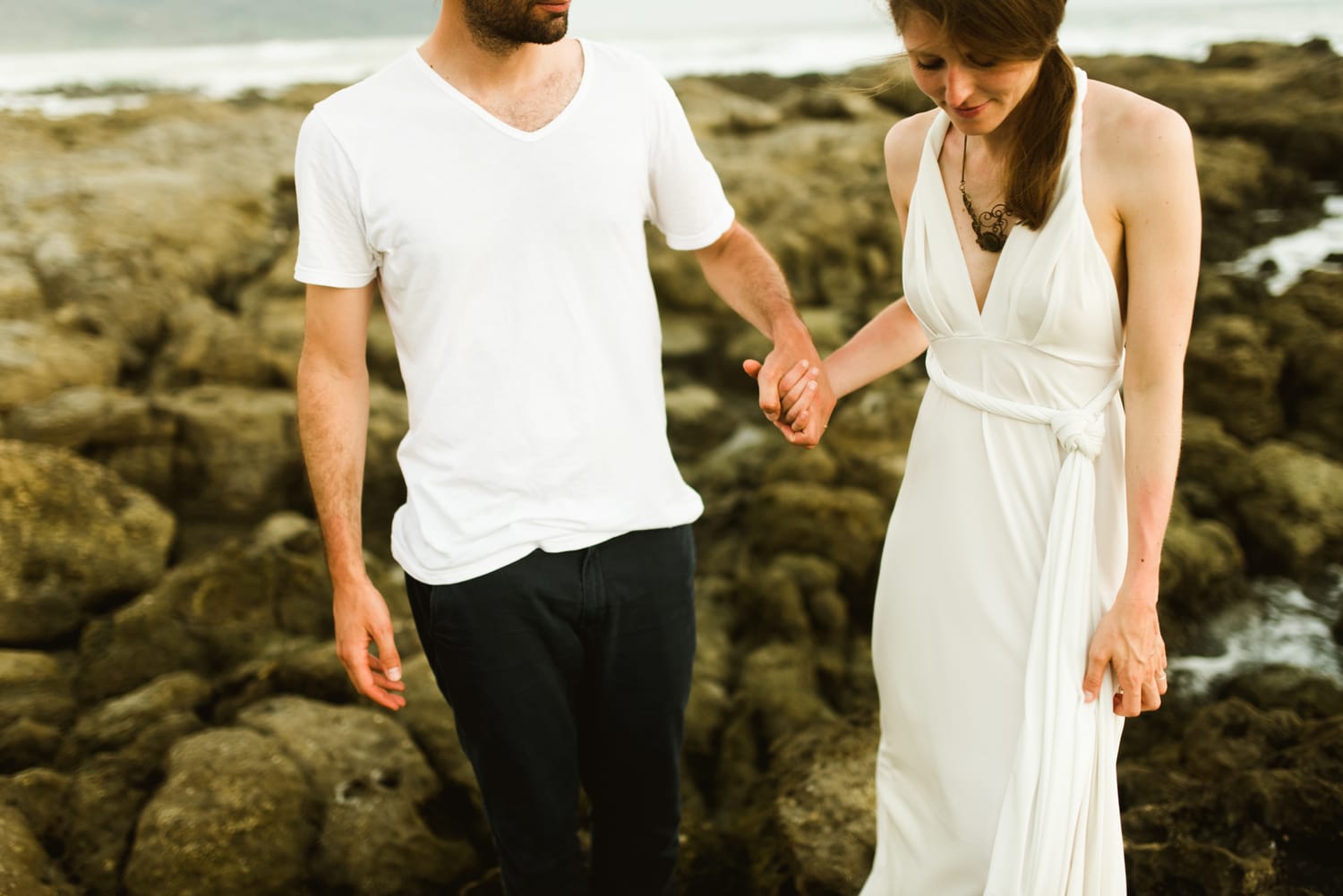 Bride and groom hold hands while standing on rocks along the shore in Santa Teresa, Costa Rica.