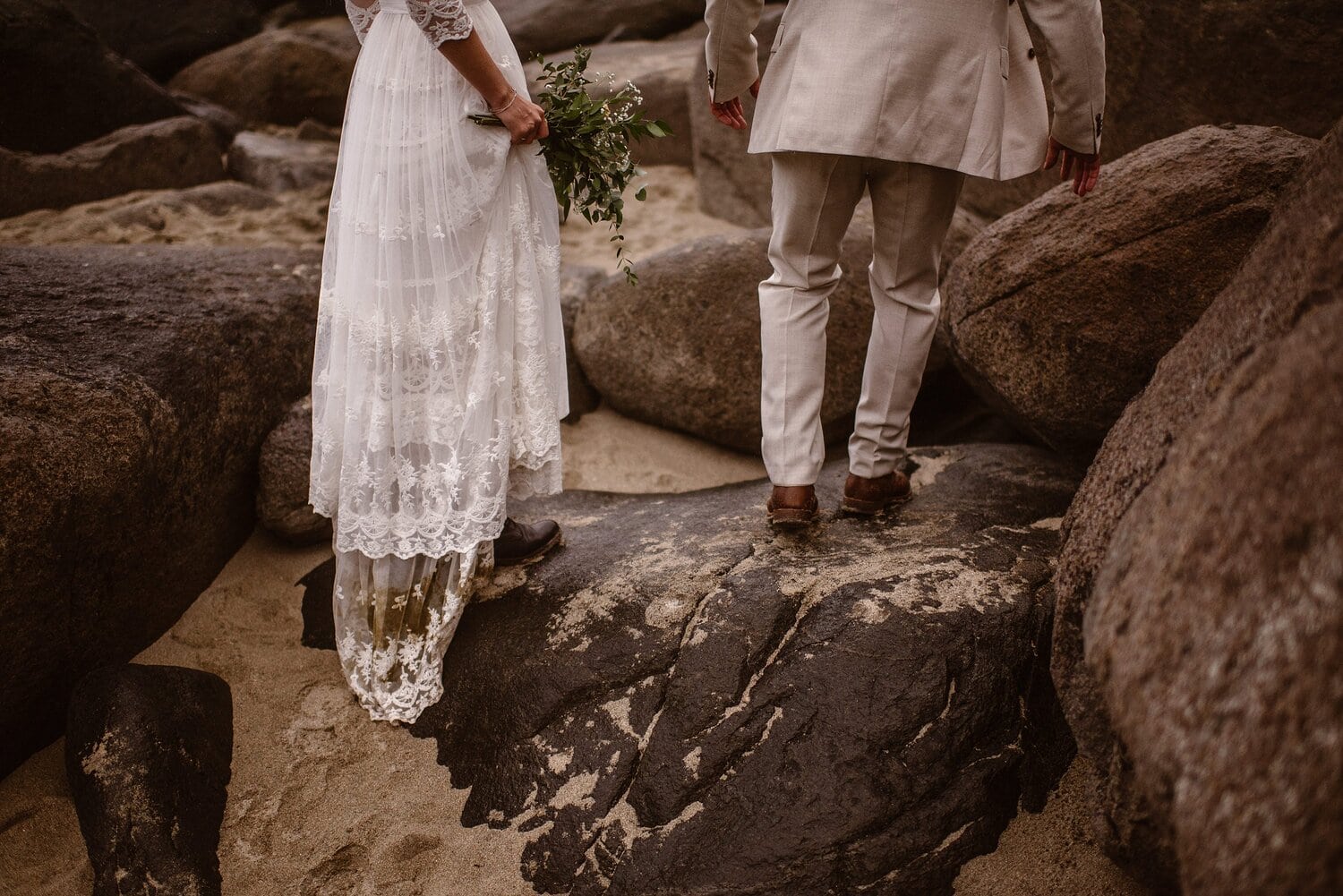 Bride and groom walk across rocks on the beach in Norway.