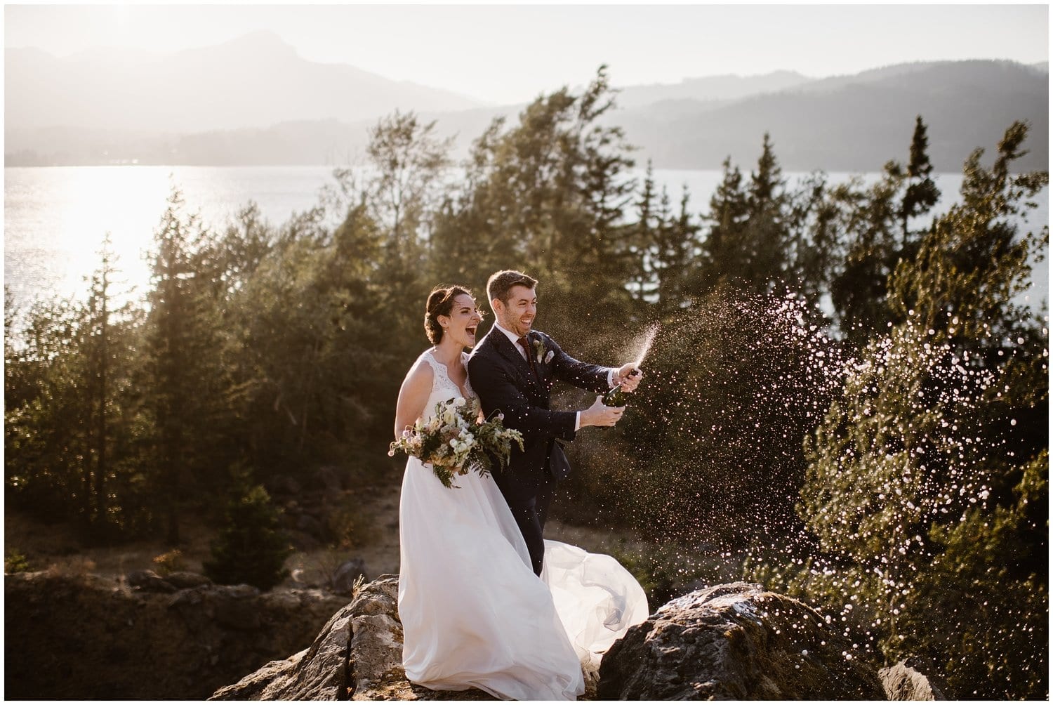 Bride and groom pop champagne while standing on coastal rocks at the Columbia River Gorge in Oregon. 