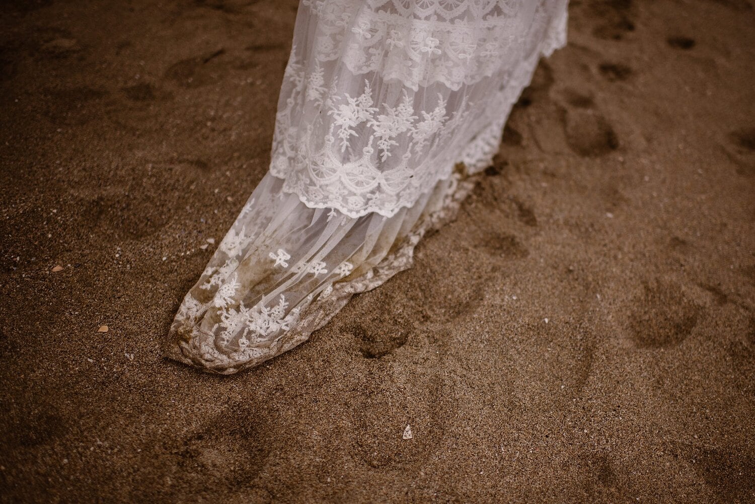 The train of the bride's white, embroidered dress covered in sand from the beach. 