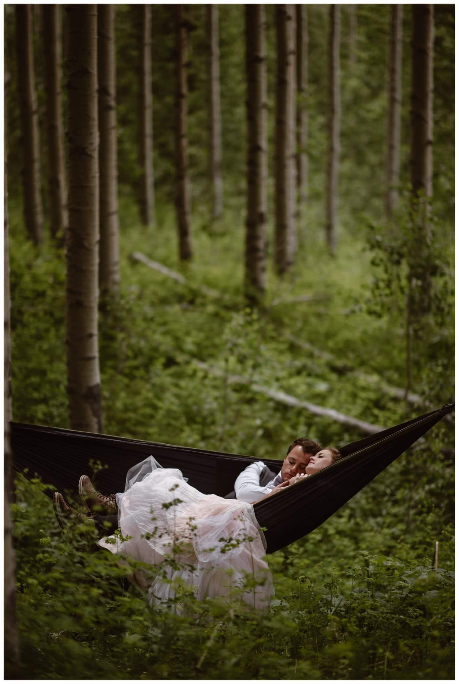 Bride and groom cuddle up in a hammock, in an aspen forest near the Maroon Bells, in Colorado. 