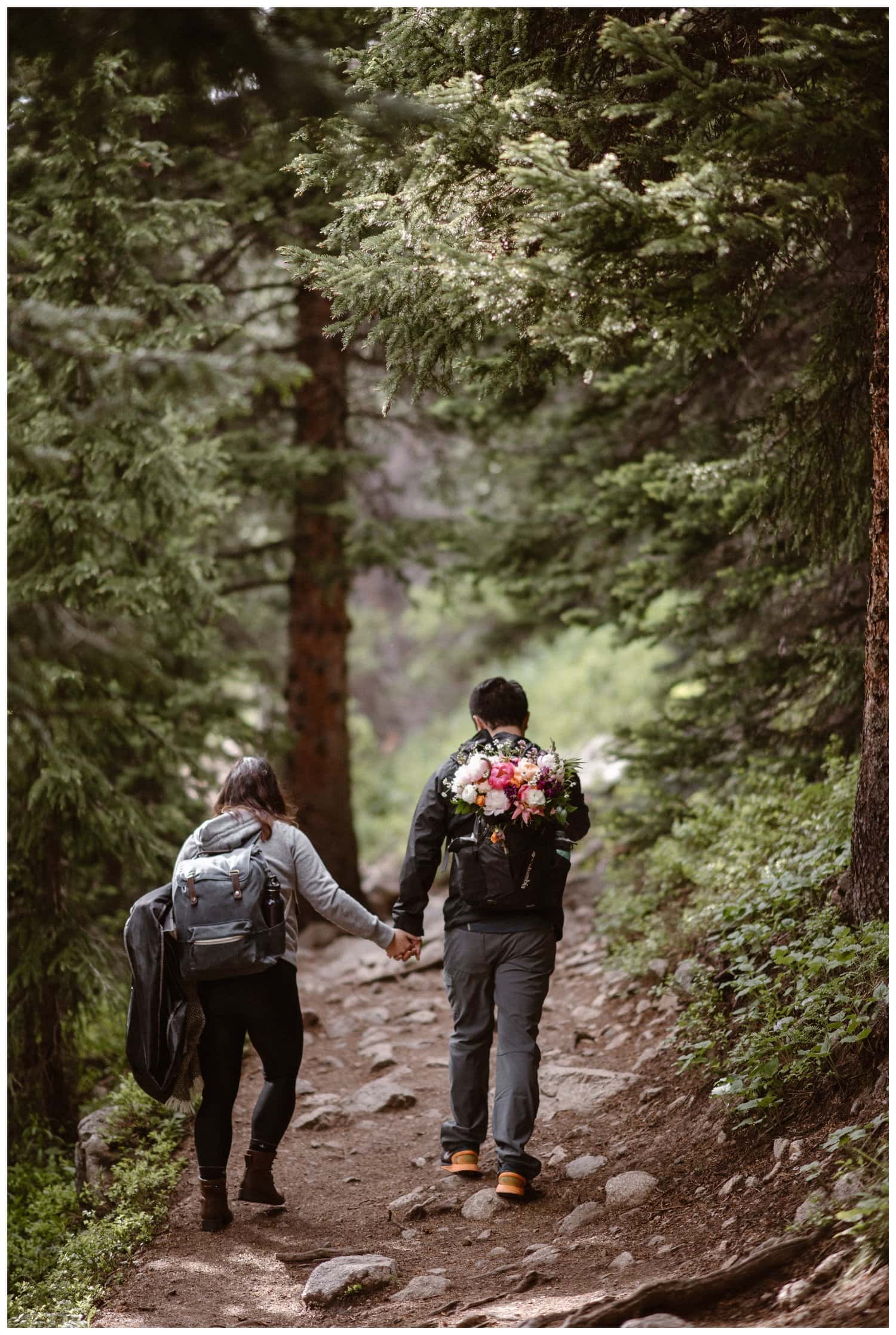Bride and groom hold hands while hiking on a trail near Boulder, Colorado on their elopement day. 