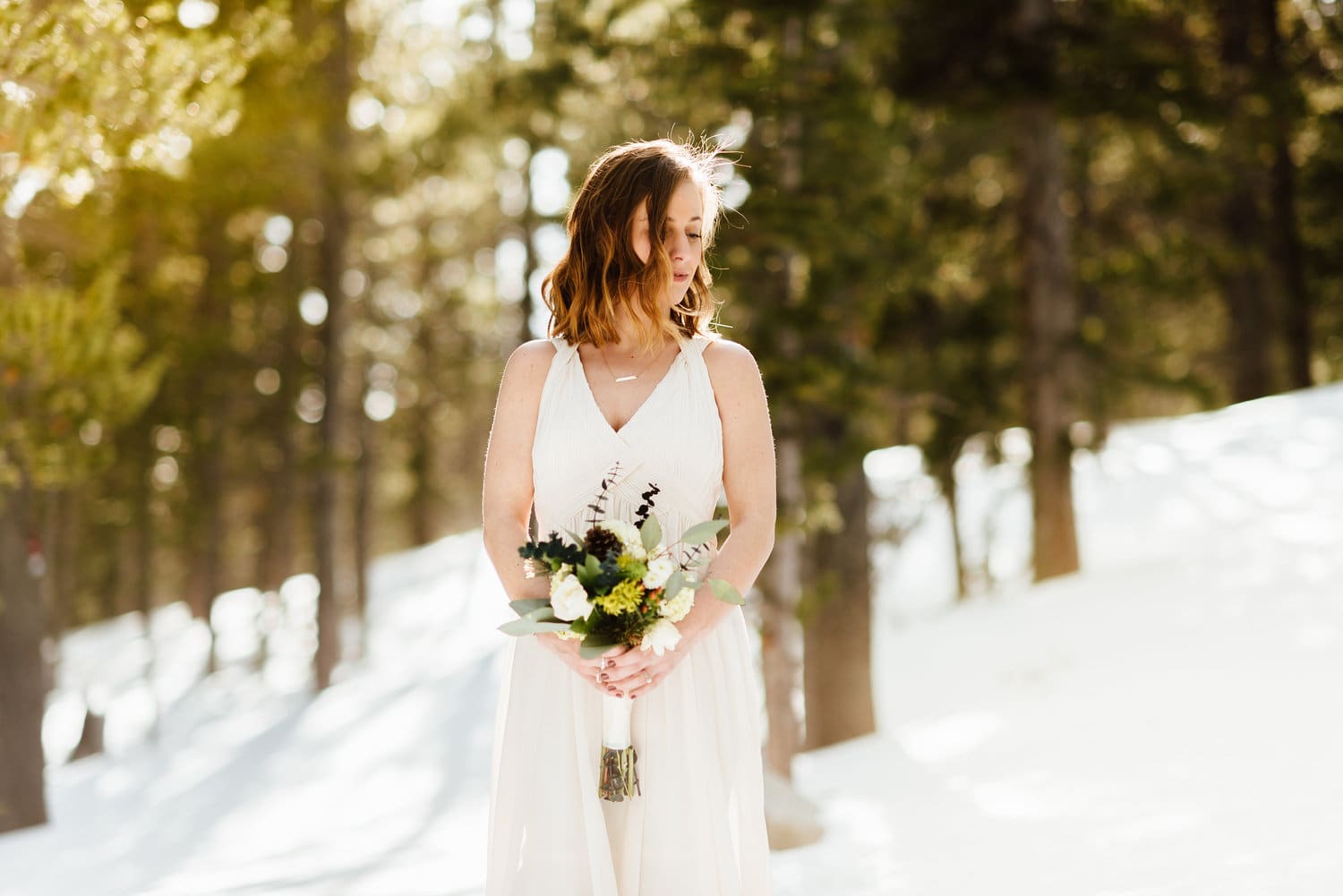 Bride wearing a white dress, holding a bouquet, surrounded by snow at St. Mary's Glacier in Idaho Springs, Colorado. 