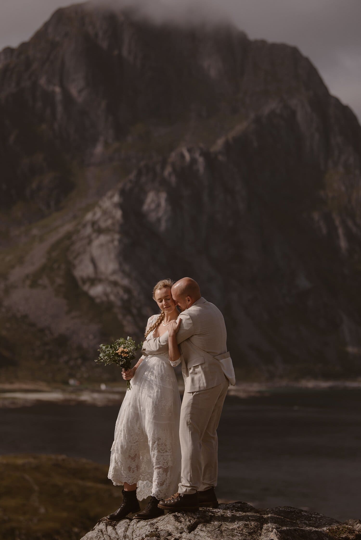 Bride and groom embrace while standing on a coastal rock next to a beach in Norway.