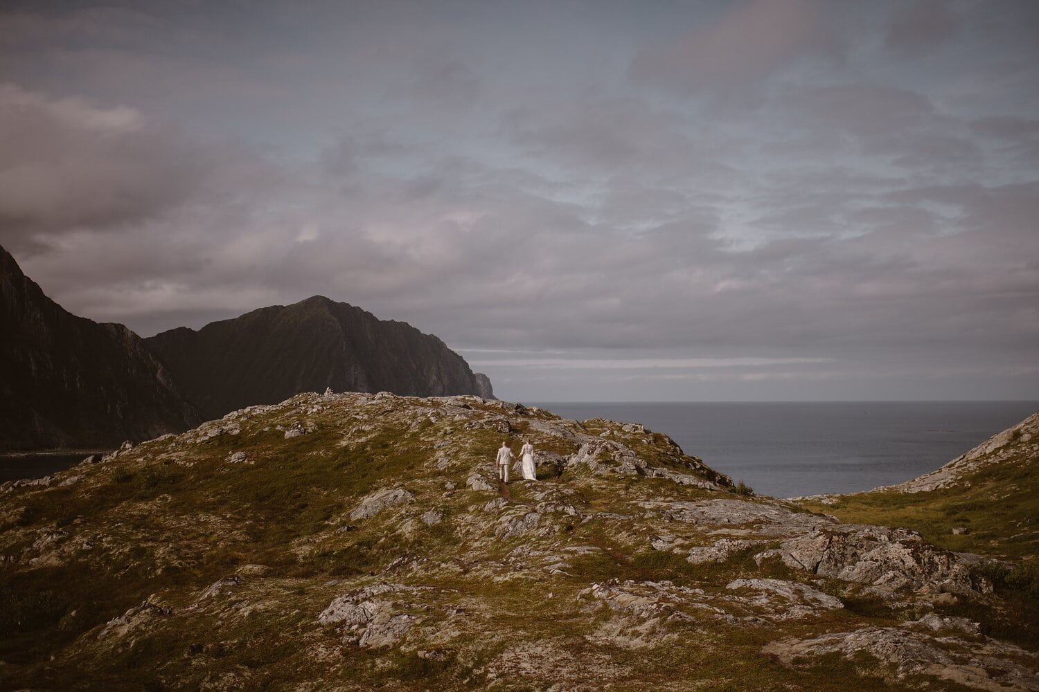 Bride and groom walk along coastal rocks on their elopement day in Norway.