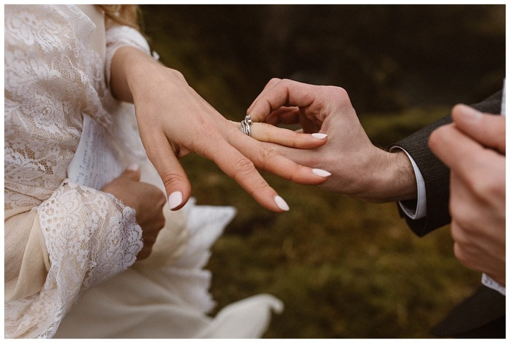 Close-up of groom placing diamond ring on brides finger. 