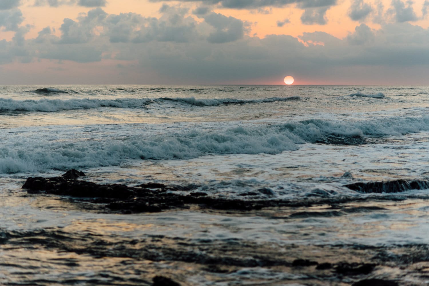 Landscape of ocean waves and sun at sunset in Santa Teresa, Costa Rica.
