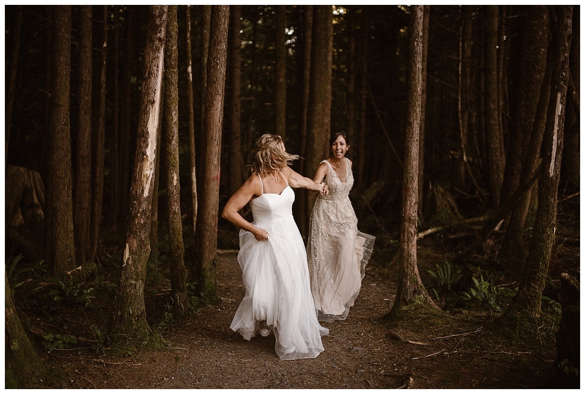 Two brides hold hands and run through a forest in Tofino, Canada. 