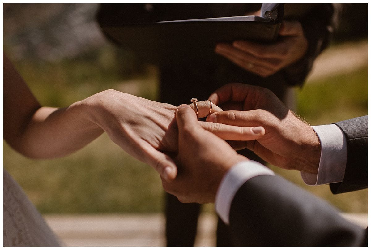 Close-up of groom placing gold ring on brides ring finger. 