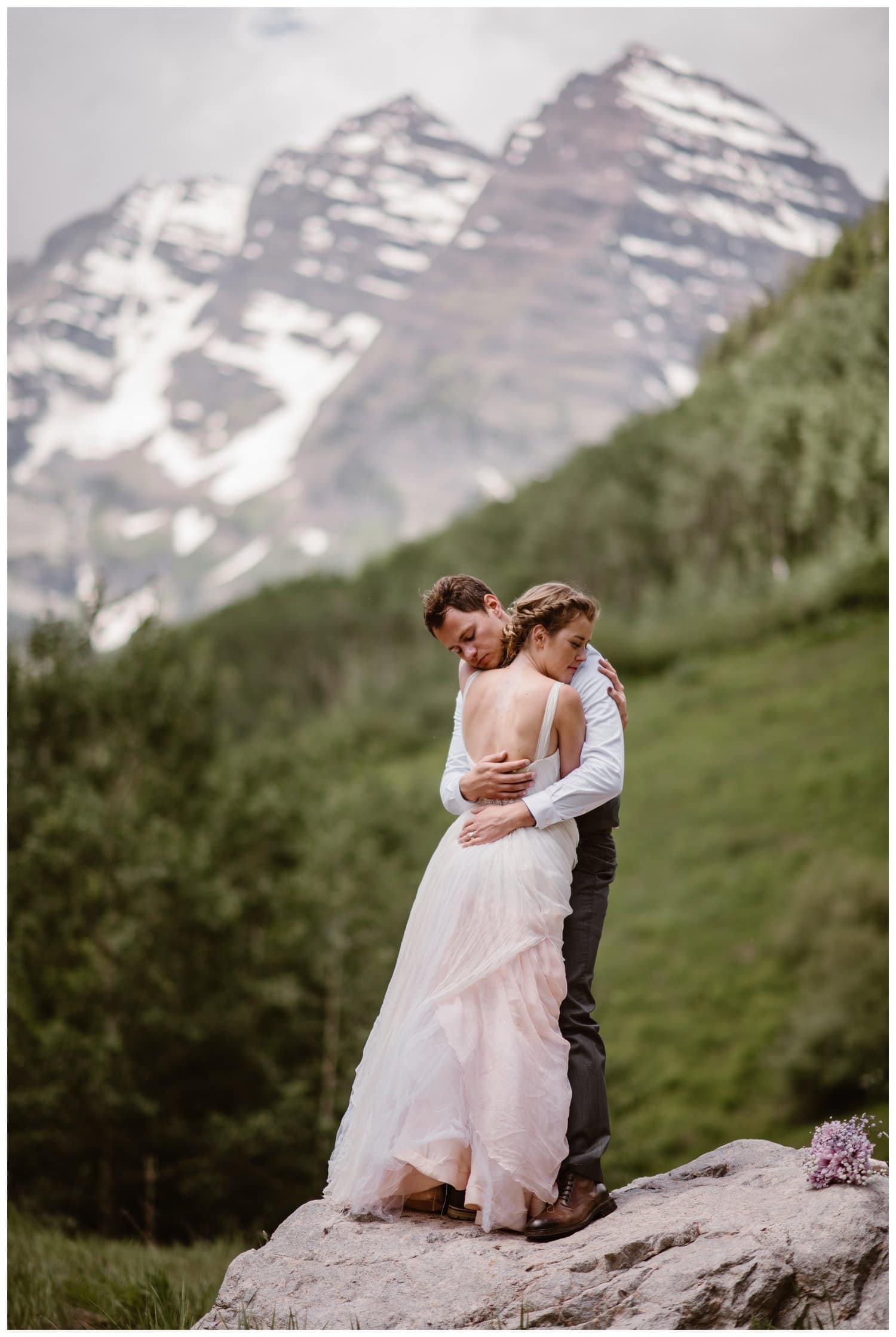 Bride and groom embrace while standing on a rock — on their elopement day near the Maroon Bells, in Colorado. 