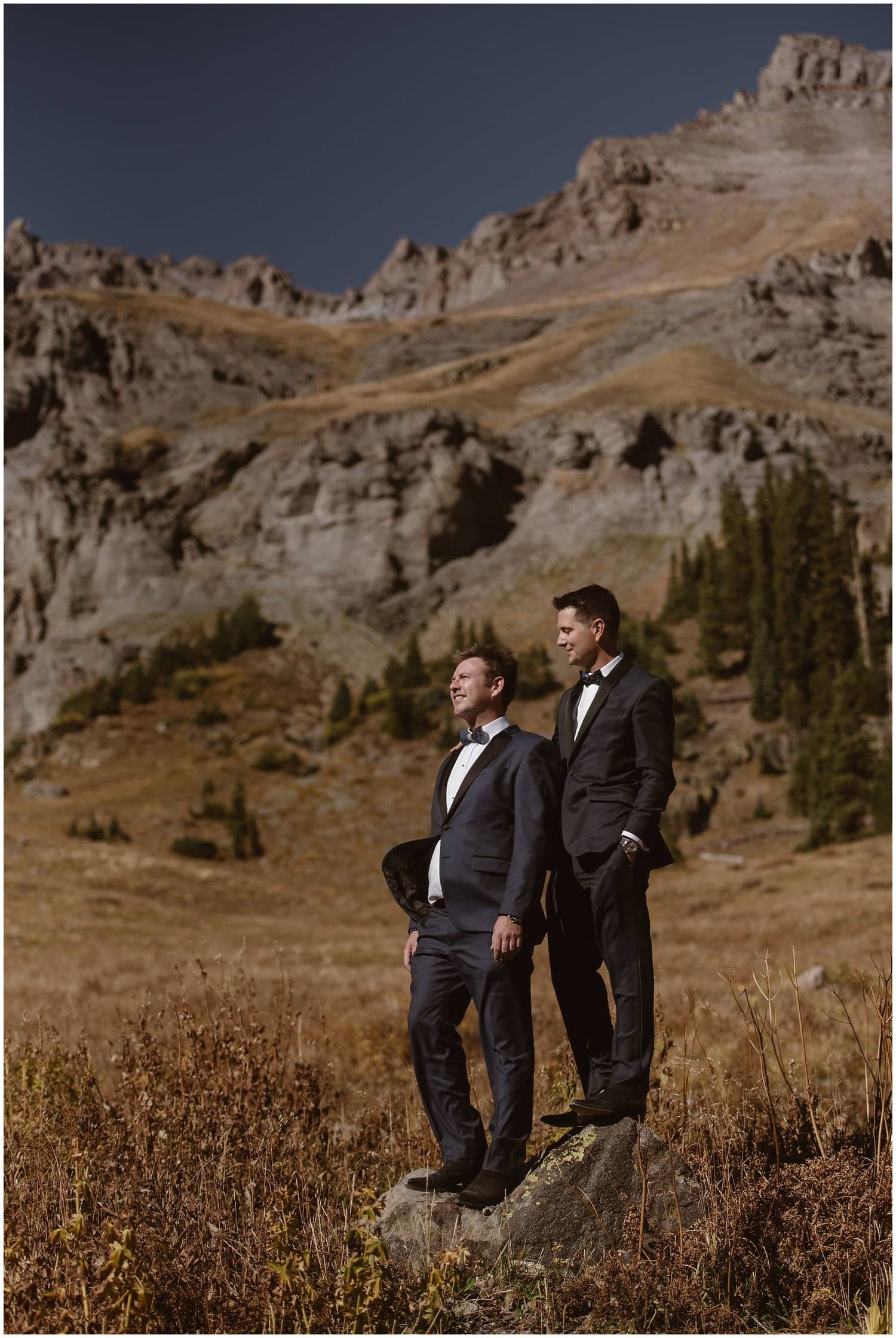 Two grooms stand on rock in valley. 