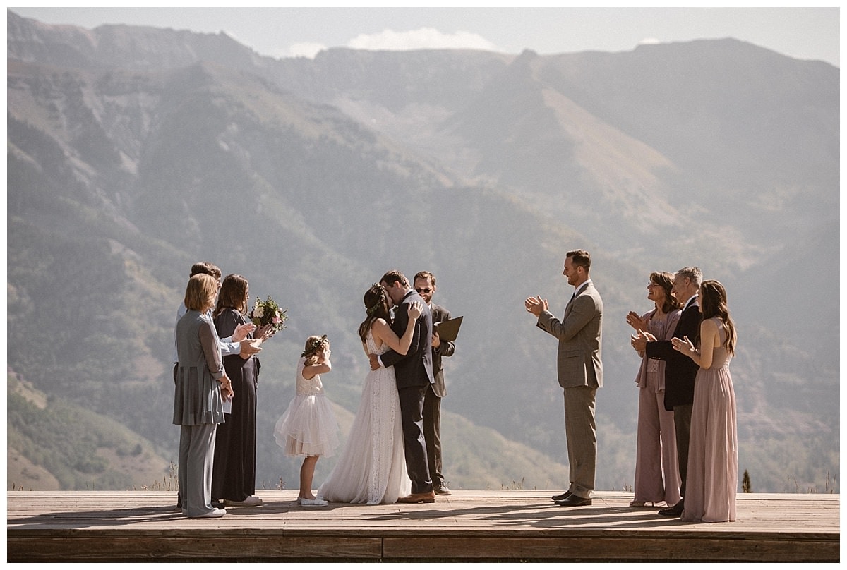 bride and groom share a kiss, surrounded by friends and family during their intimate elopement ceremony at the San Sophia Overlook
at Telluride Ski Resort in Colorado. 