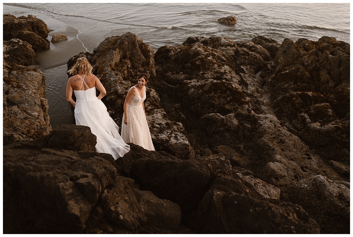 Two brides stand on rocks along the shore in Tofino, Canada. 