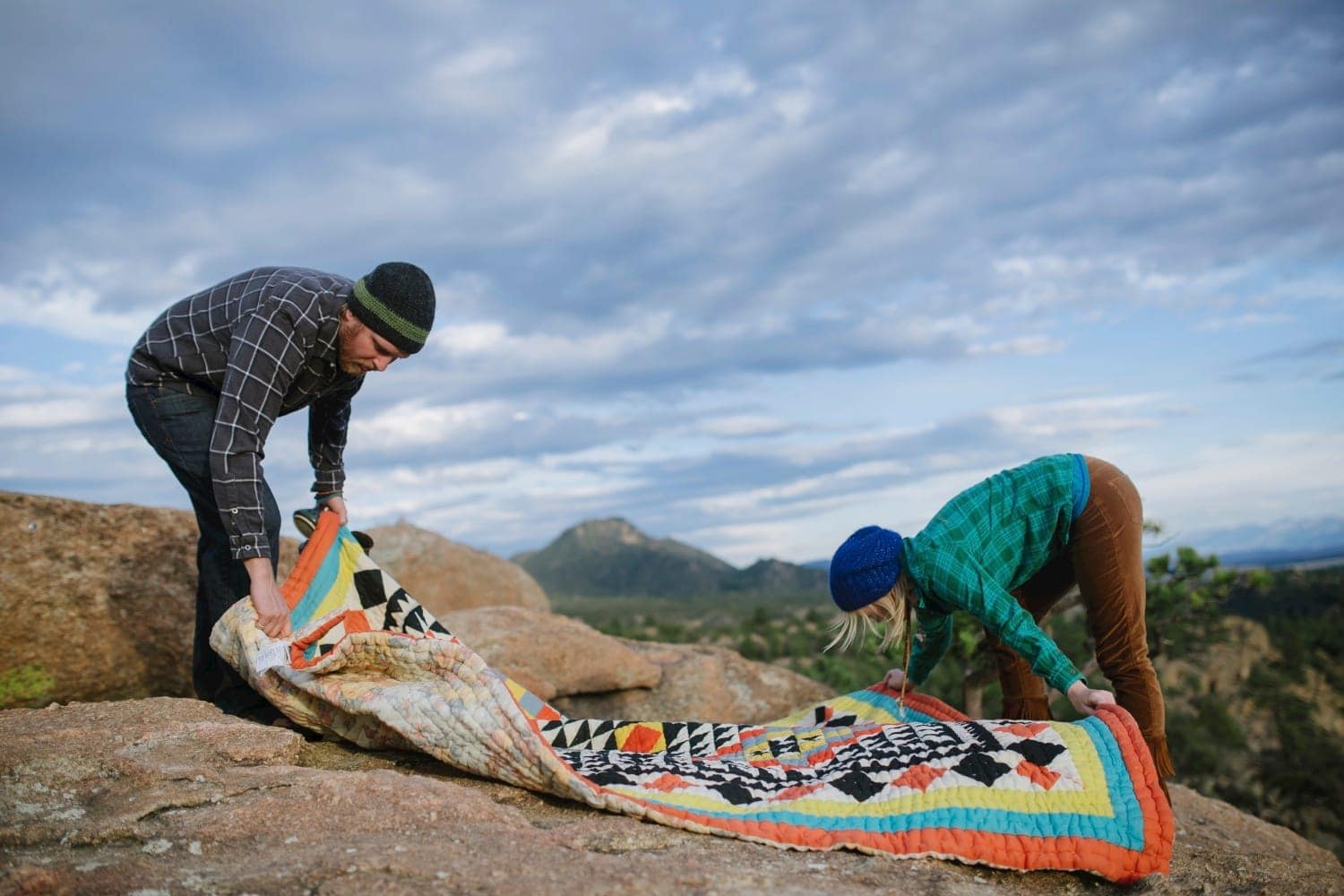 Couple laying down a picnic blanket together, with mountains in the background, in Buena Vista, Colorado. 