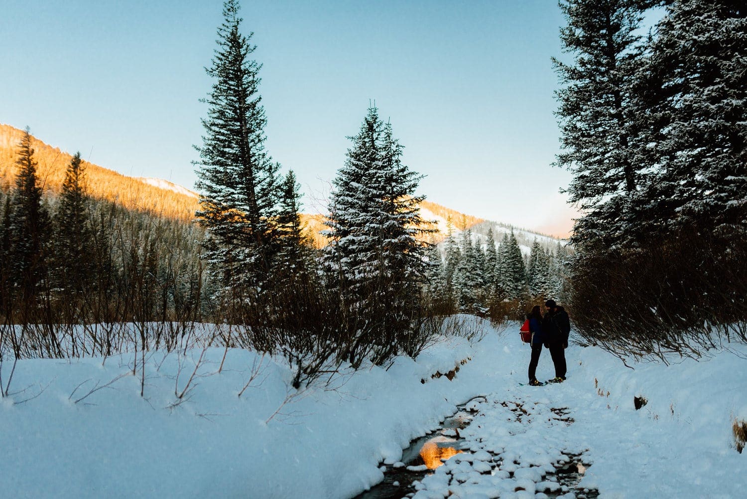 Couple snowshoeing at Indian Peaks, in Colorado. There is snow covering the ground and a forest in the background. 