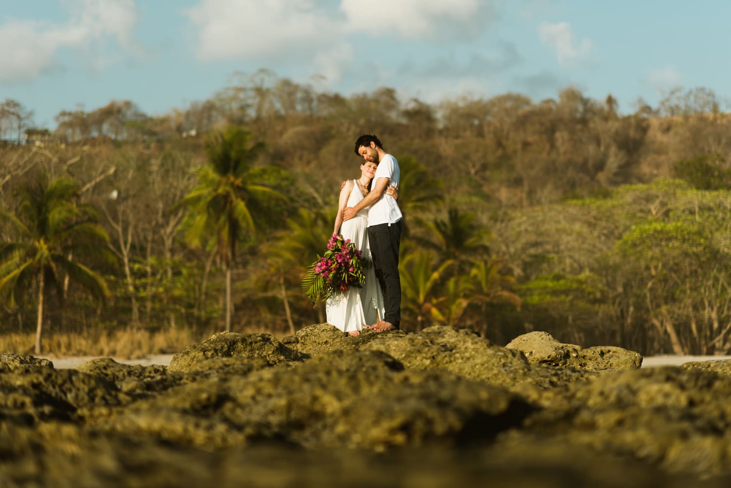 Bride and groom embrace with standing on rocks along the shore in Santa Teresa, Costa Rica.