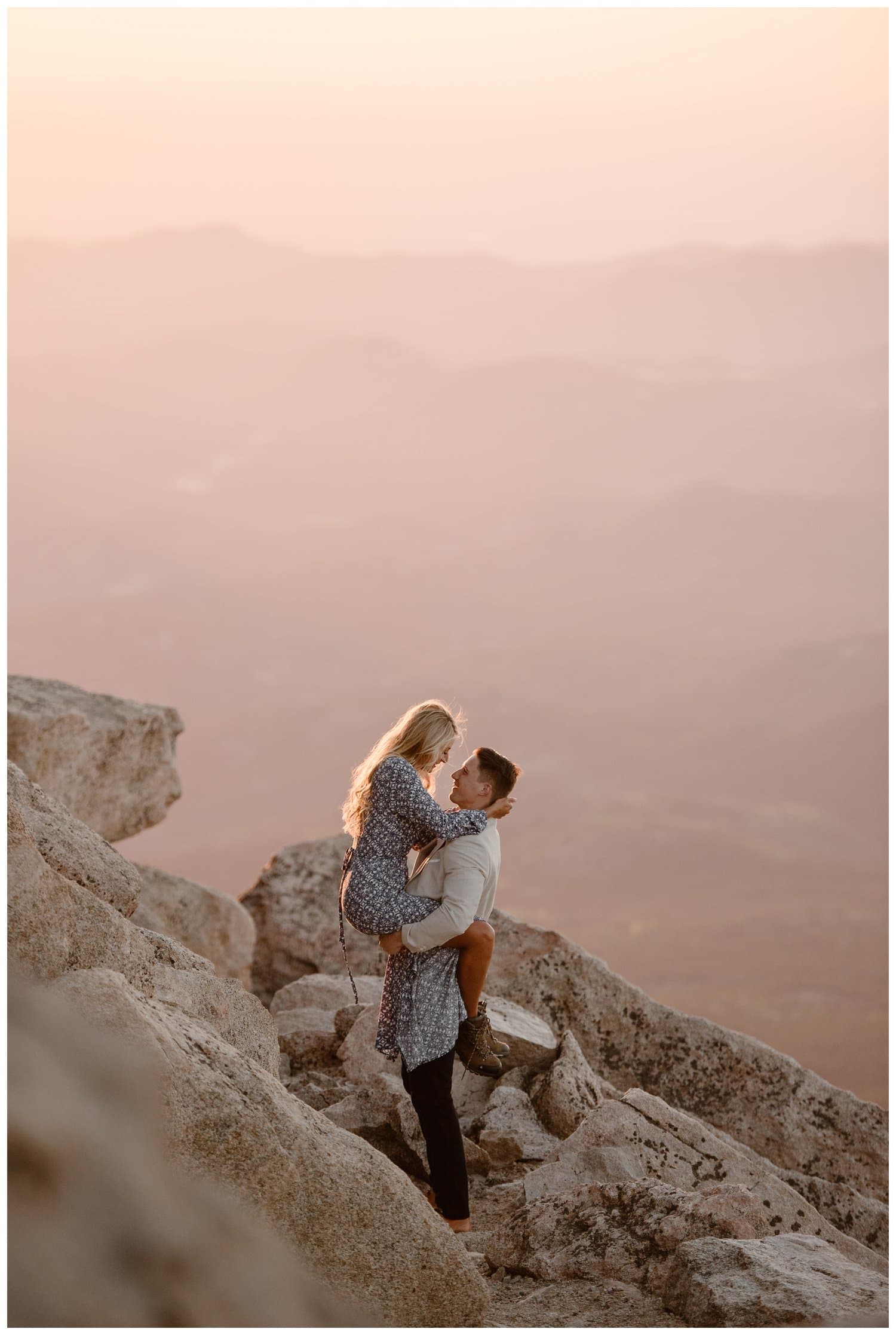 Man holds woman and they are smiling at each other, at the top of Mt. Evans in Colorado.