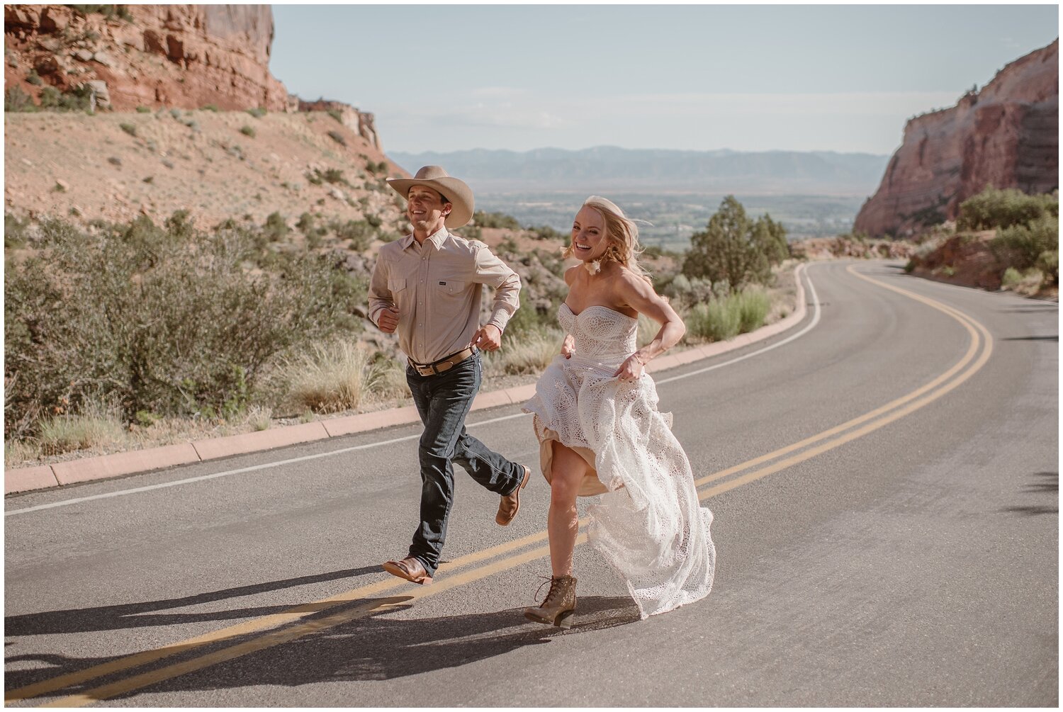 Bride and groom run together on road at Colorado National Monument. 