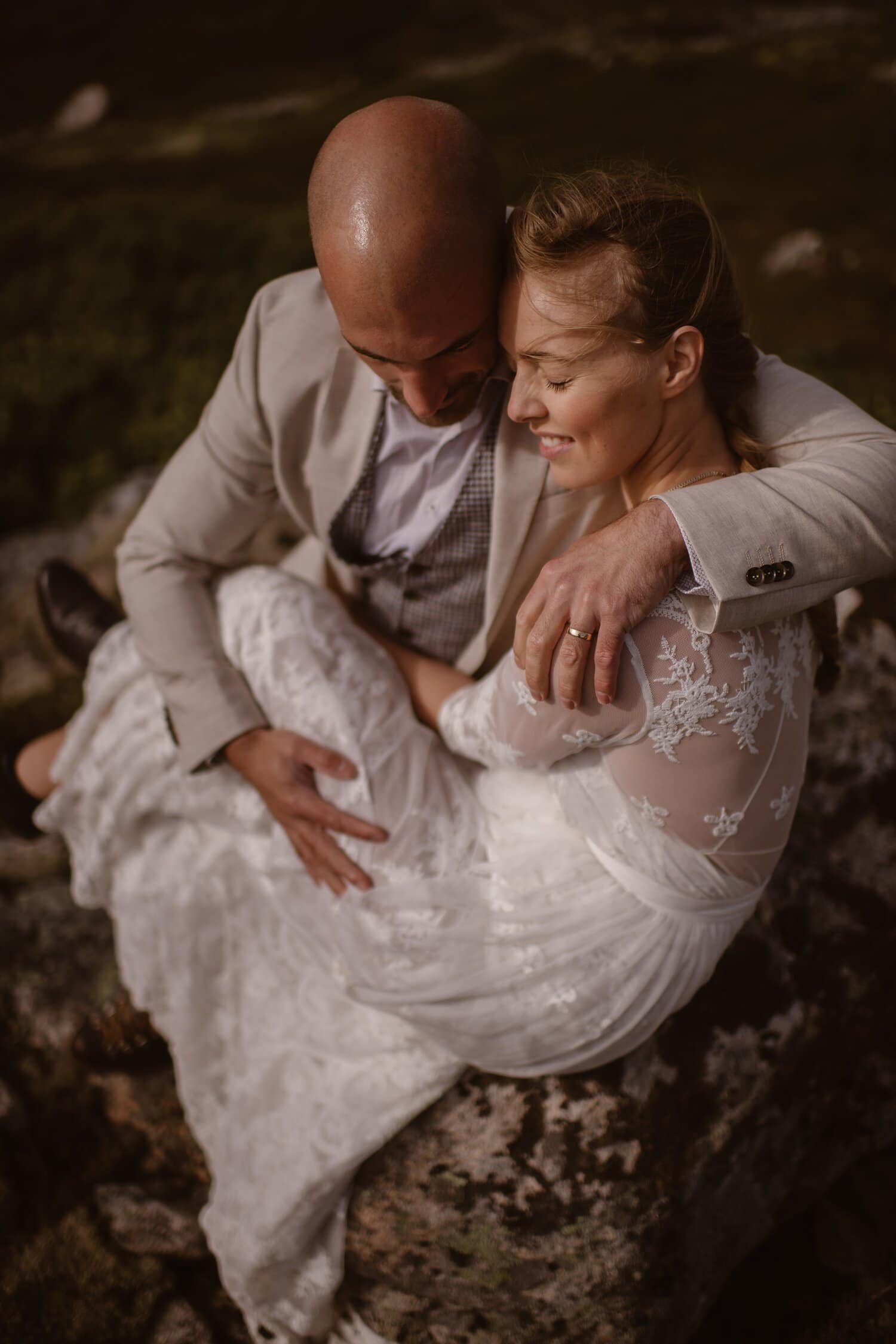 Bride and groom embrace while sitting on a rock together at the Lofoten Islands in Norway.