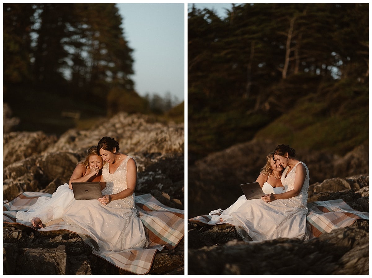 Two brides sit on a rocks near the shore and watch videos from their friends and family on their elopement day in Tofino, Canada. 
