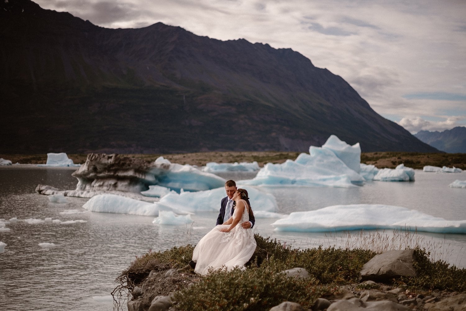 Bride and groom sit together in front of Knik Glacier in Alaska on their elopement day. 