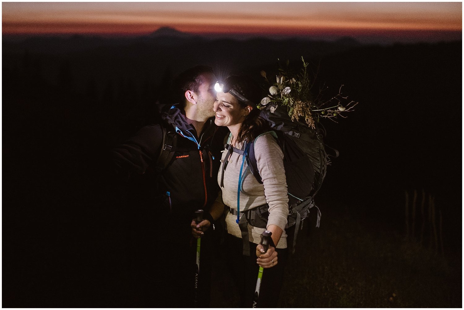 Groom kisses the bride on her cheek during a sunrise hike. Her headlamp lights up their faces. 