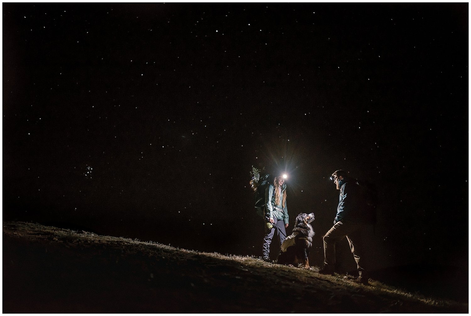 Bride and groom with headlamps, and their dog, at night. There are stars in the background. 