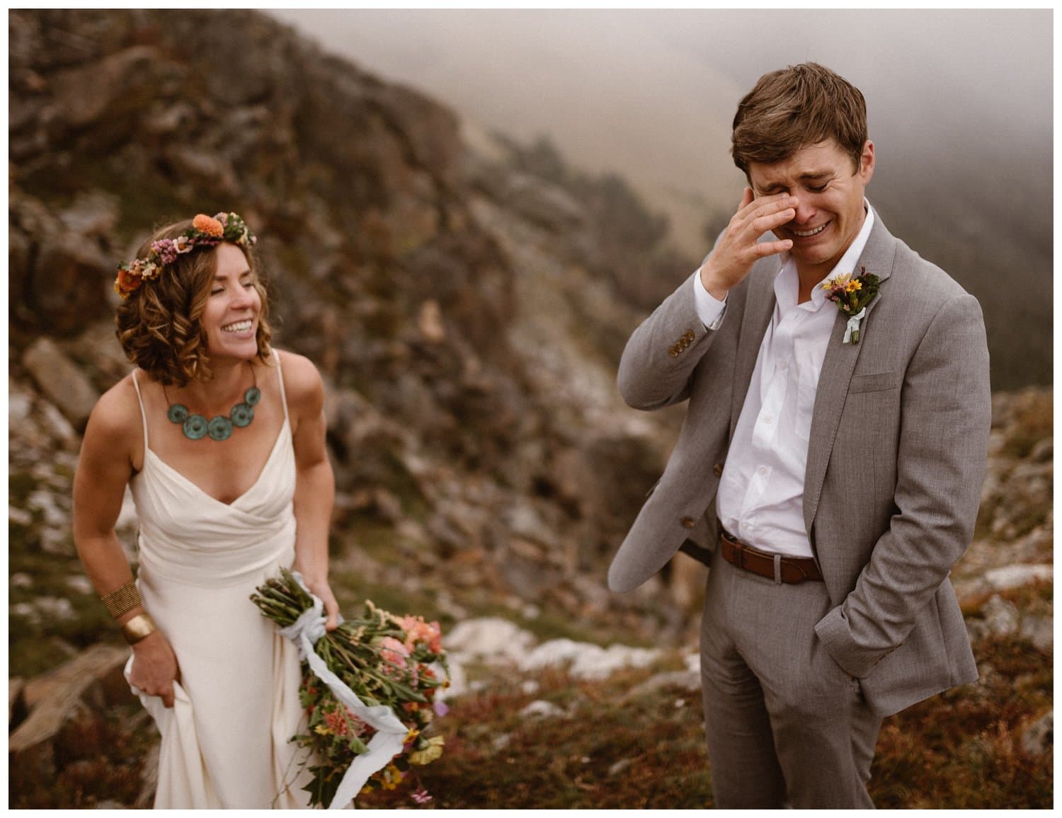 Bride and groom share an emotional first look on their elopement day. The bride is wearing a white dress, holding a bouquet, and wearing a matching flower crown. The groom is wearing a grey suit. 