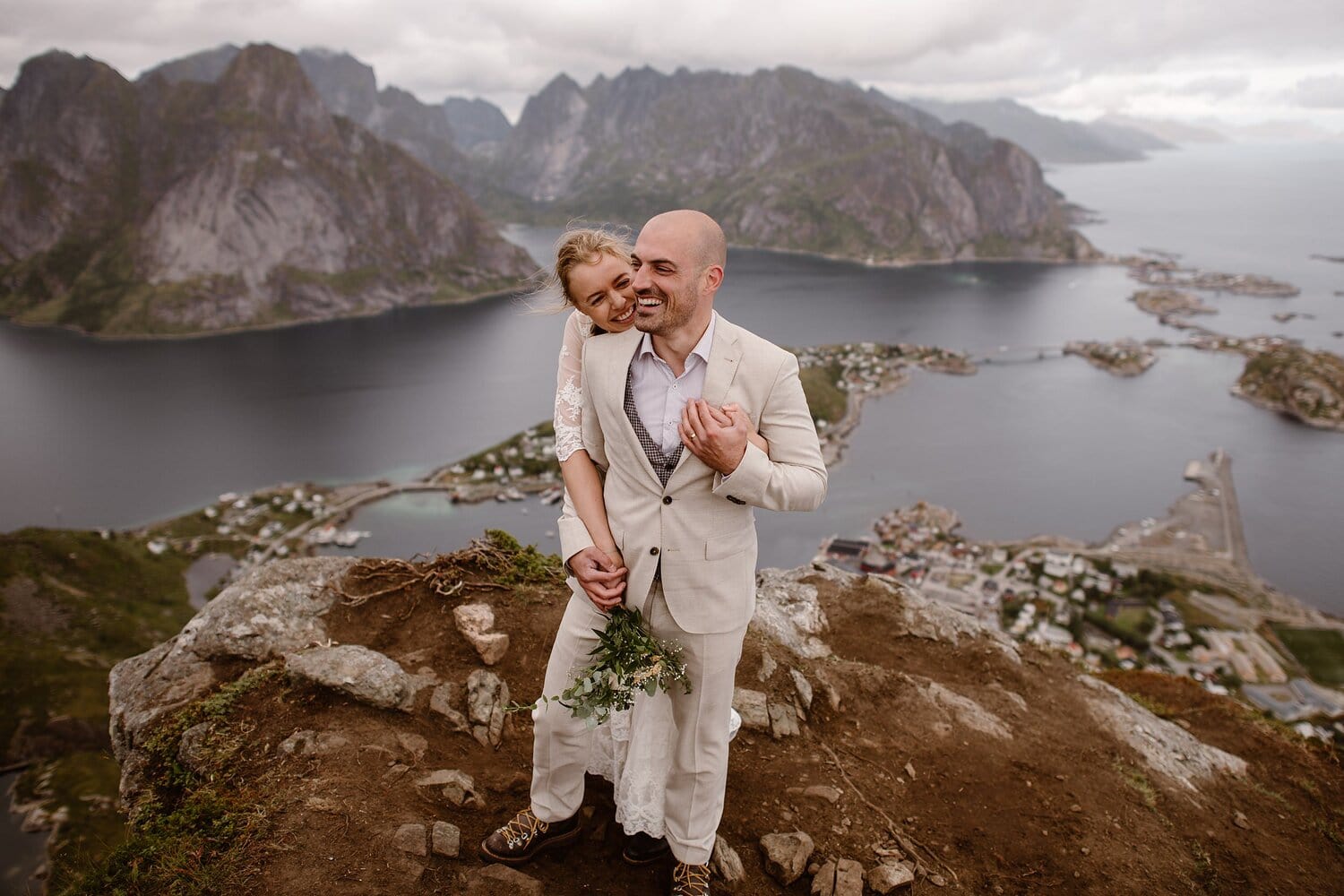 Bride and groom laughing while standing on a cliff at the Lofoten Islands in Norway.