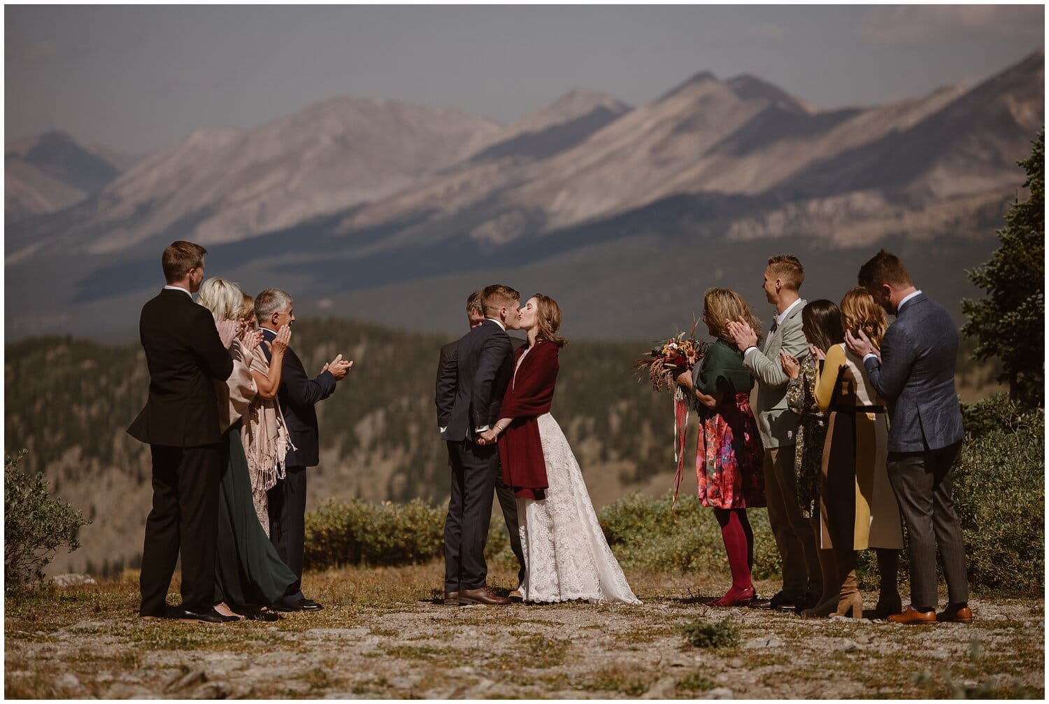Bride and groom kiss while their families surround them during an intimate ceremony, with mountains in background, in Buena Vista Colorado. 