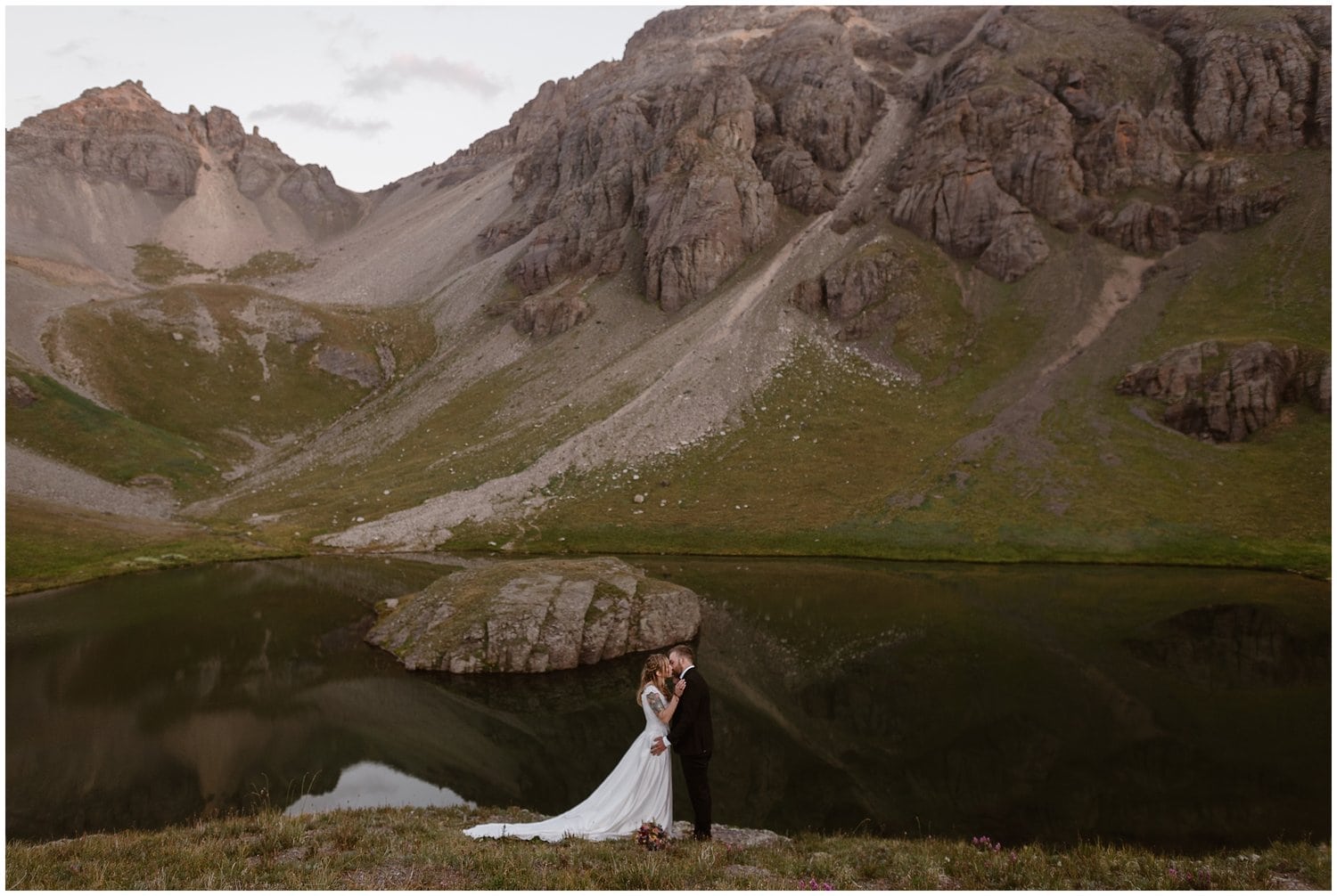 Bride and groom share a kiss in front of alpine lake, during all-day elopement in Colorado. 