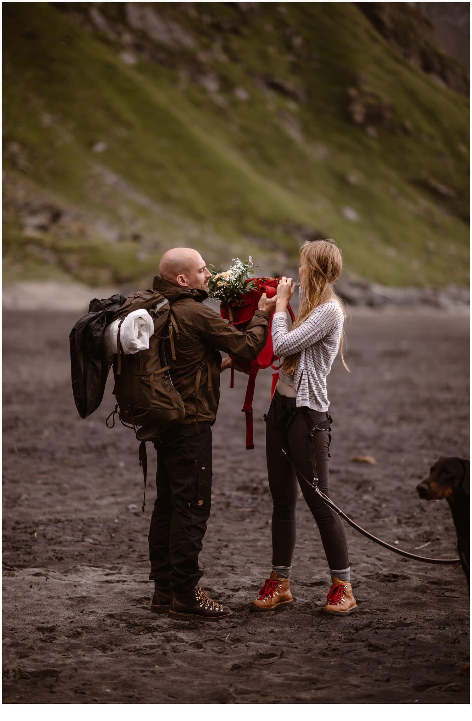 Groom is helping the bride take off her backpack on a beach in Norway.