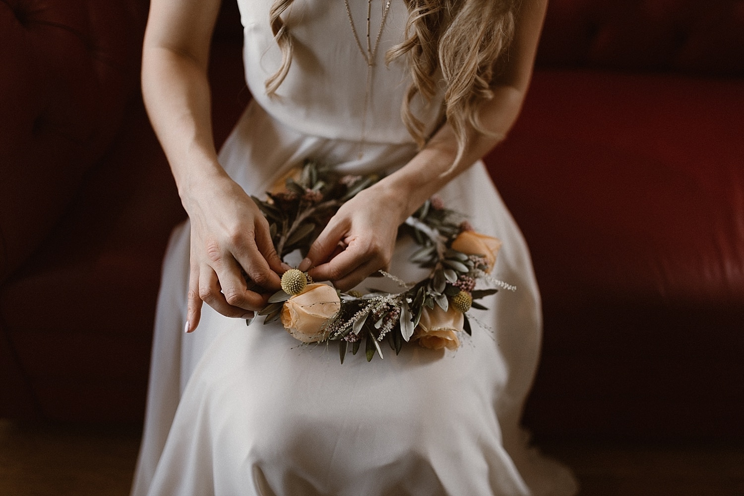 Close-up of bride adjusting her flower crown, with peach colored roses and greenery. 
