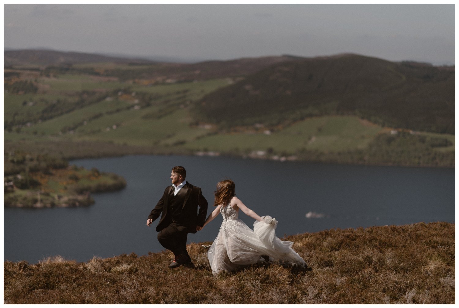 Bride and groom hold hands and run along a ridge overlooking Loch Ness in the Scottish Highlands. 