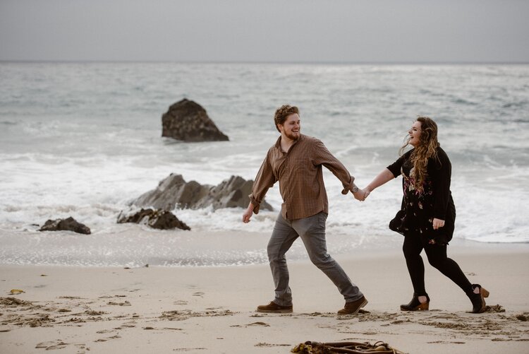 Bride and groom hold hands and walk along the beach on their elopement day in Big Sur, California.