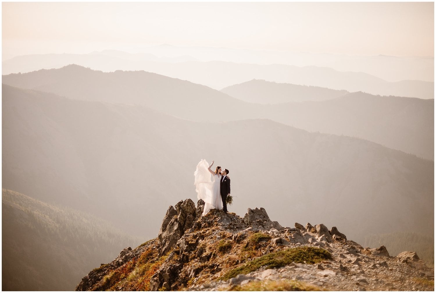 Bride and groom with their arms around each other, while standing on a mountain cliff in Washington at sunrise.