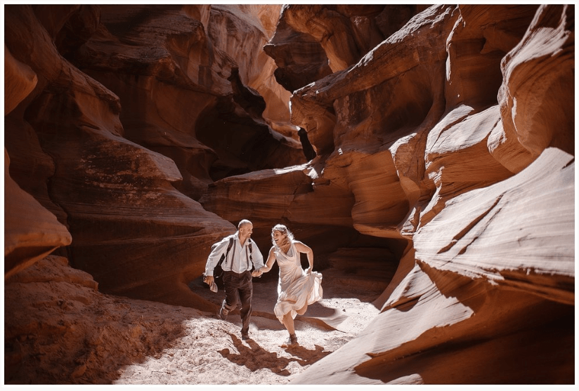Bride and groom hold hands and run through slot canyon. 