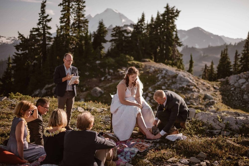 Groom washes the bride's feet during their elopement ceremony at the base of Mount Shuksan in Washinton. They are surrounded by their friends and family. 