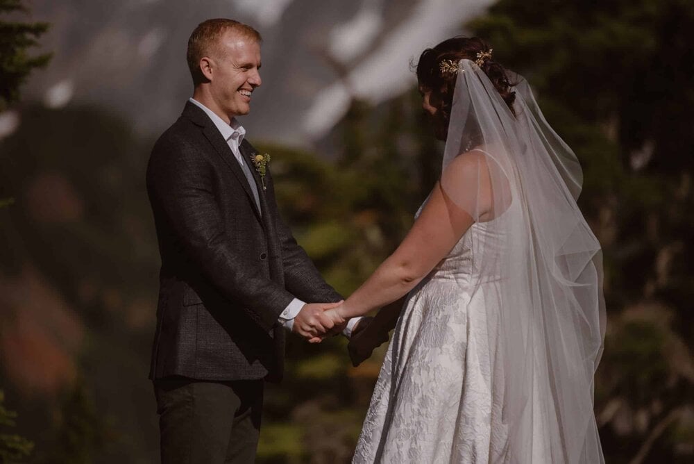 Bride and groom hold hands and smile at each other on their elopement day in at the base of Mount Shuksan in Washinton. 